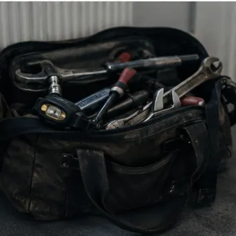 A worn toolbag on a hallway floor beside a radiator.
